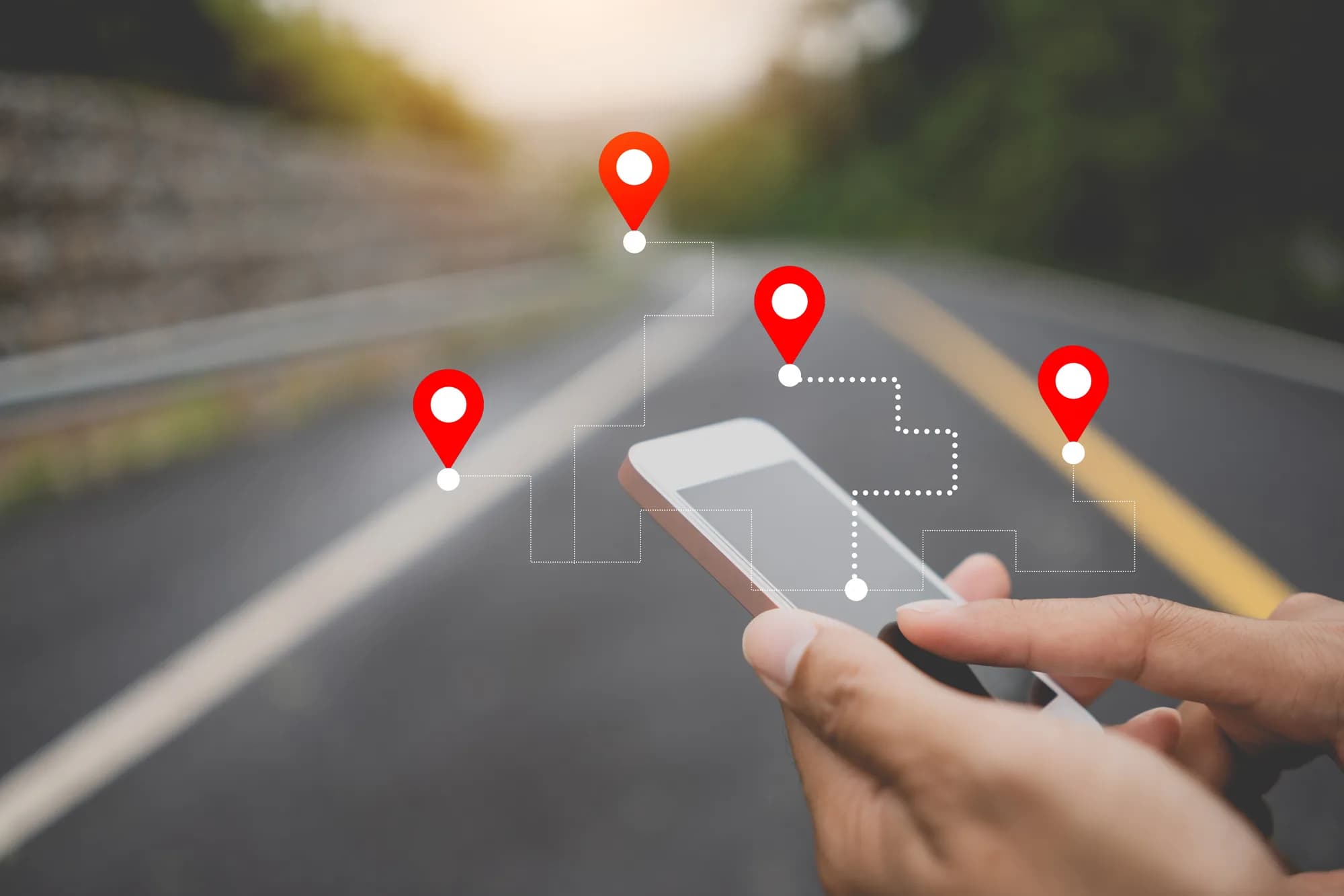 A hand holding a smartphone on a road, with map location pins floating above it