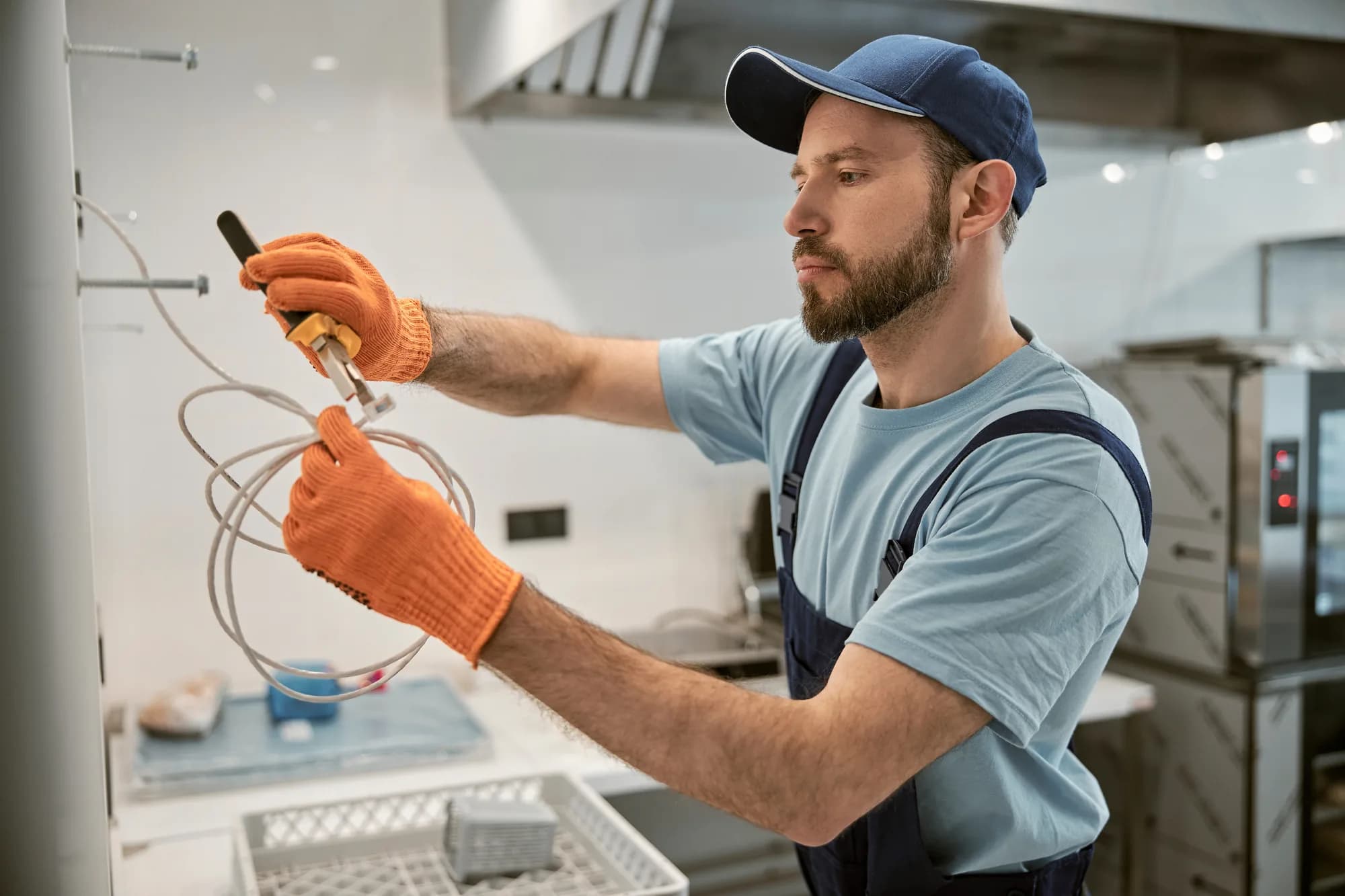 An electrician wiring an electrical outlet on the wall of a commercial kitchen