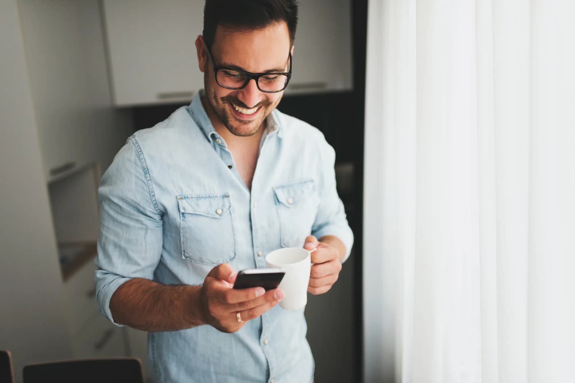 A person smiling while reading email on a phone, coffee in hand