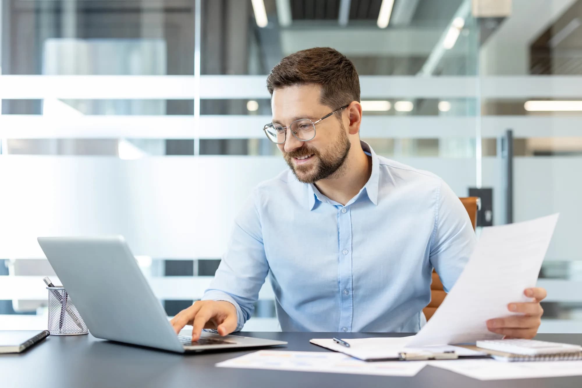 A business owner working at a laptop while reviewing printed reports