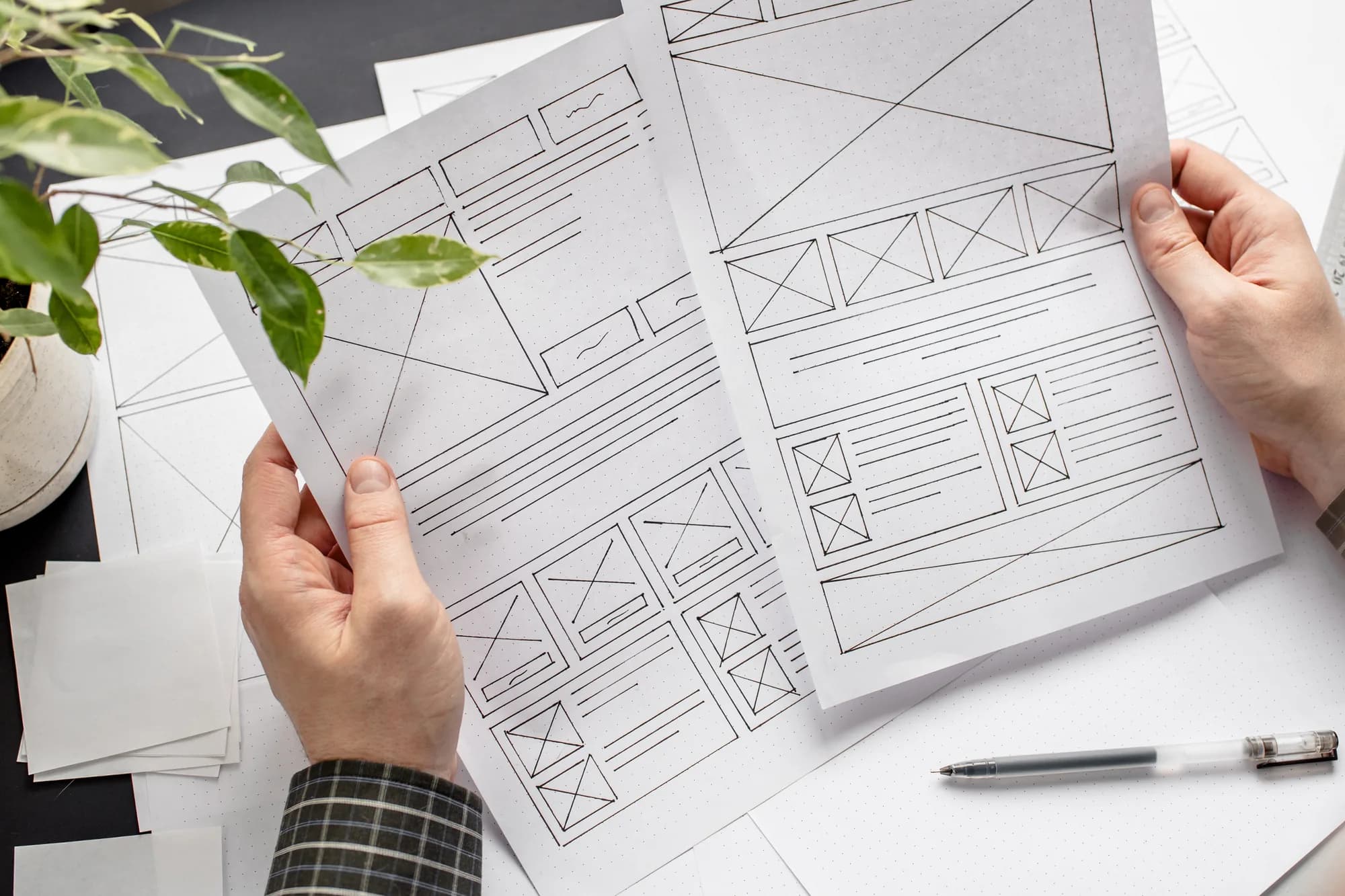 Hands reviewing printed website wireframes on a desk