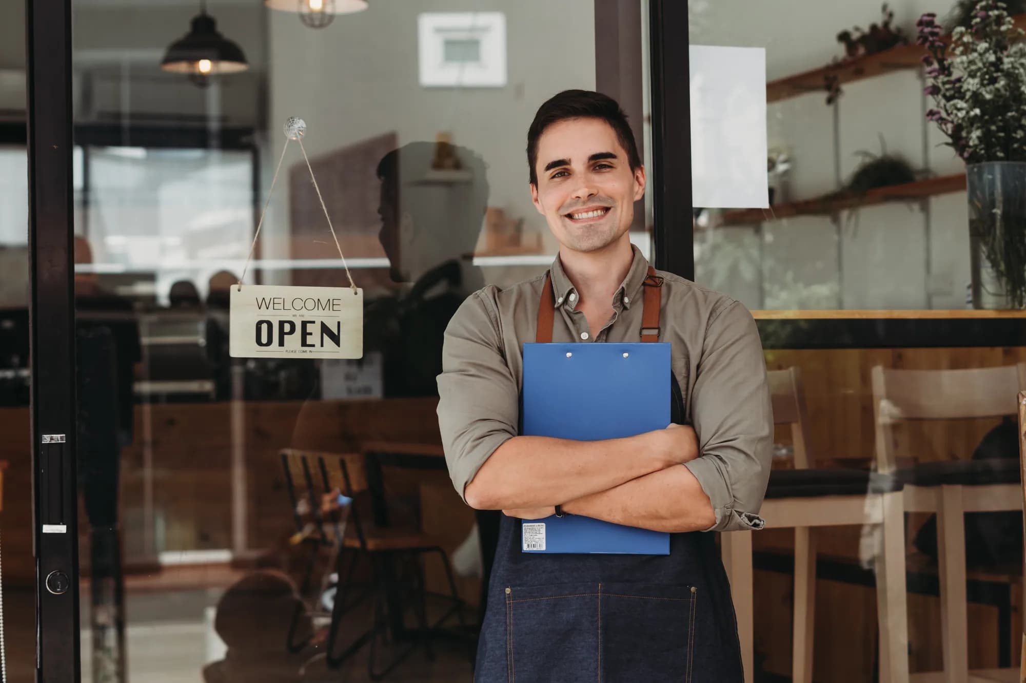 A small business owner standing outside their shop beside an open sign